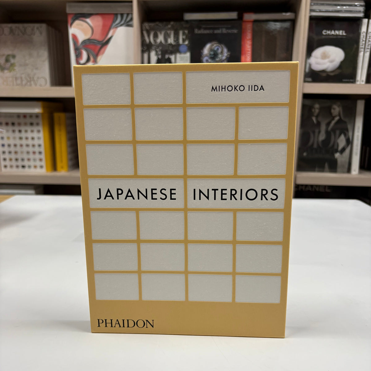 Livro Japanese Interiors de Mihoko Iida com capa dura sobre mesa de centro de madeira clara, ao lado de uma xícara de chá e u