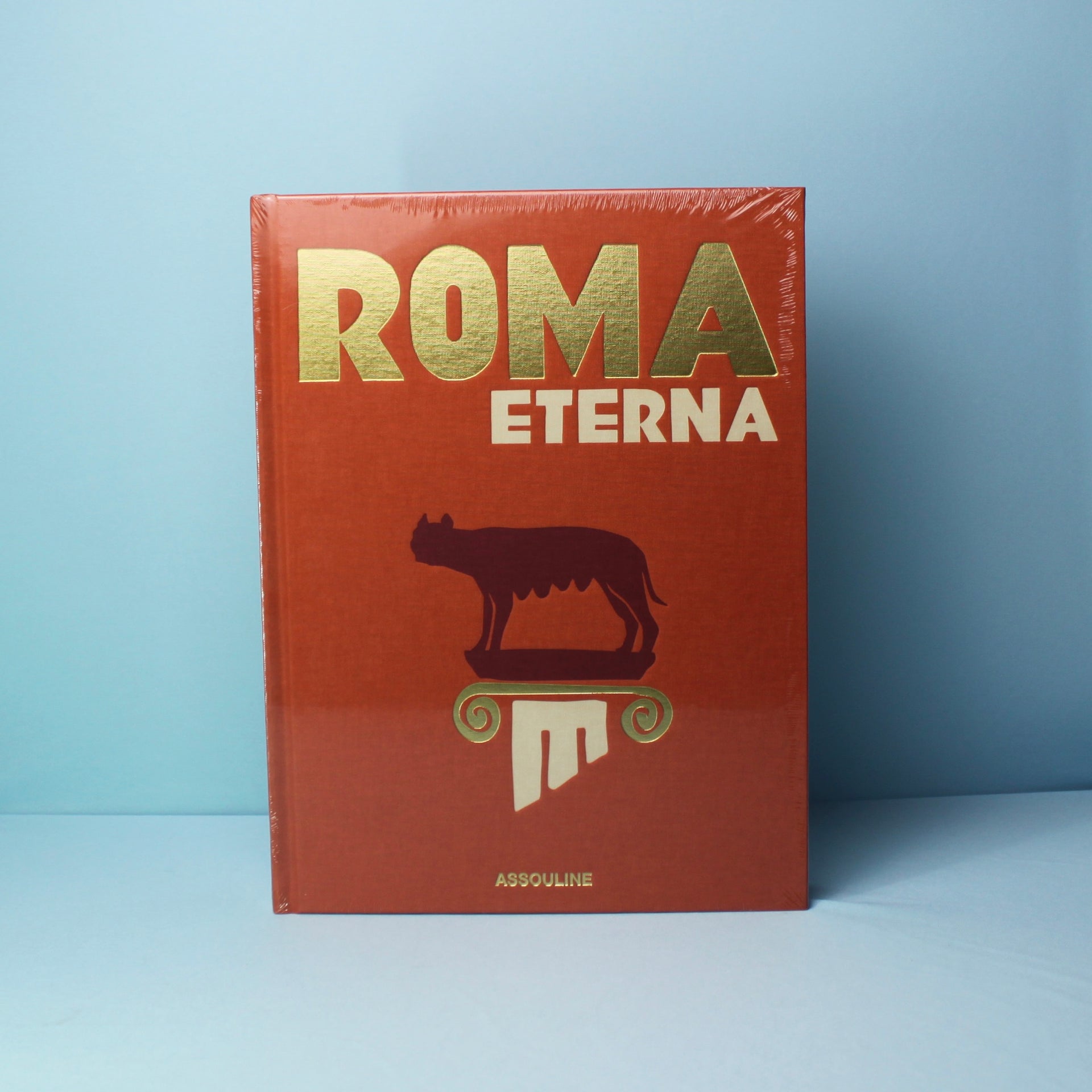 Livro Roma Eterna Assouline com capa dura sobre mesa de centro de madeira nobre, ao lado de uma escultura clássica e luz natu