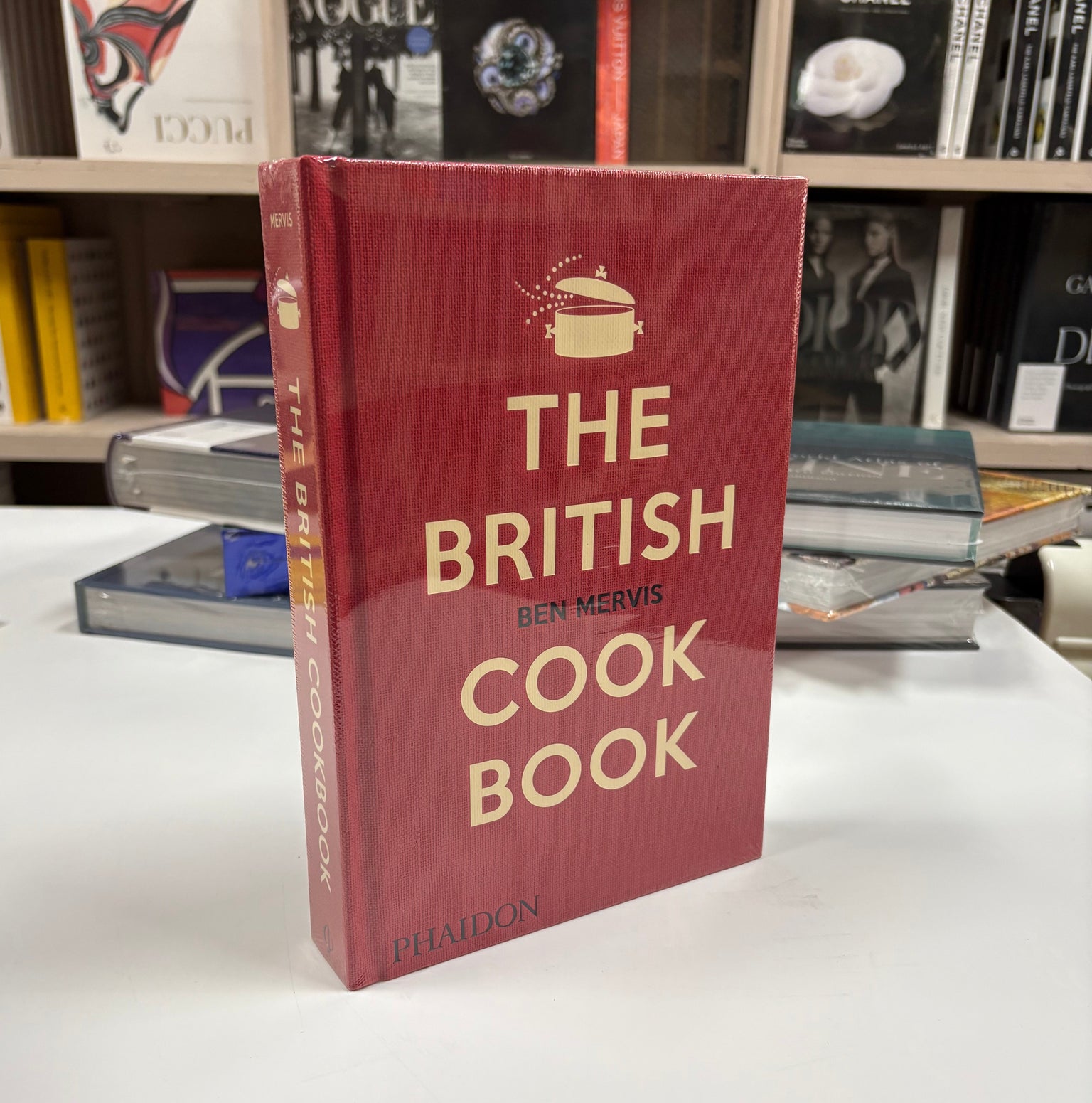 Livro The British Cookbook Phaidon Press com capa dura sobre mesa de centro em cozinha iluminada com utensílios de cobre e er