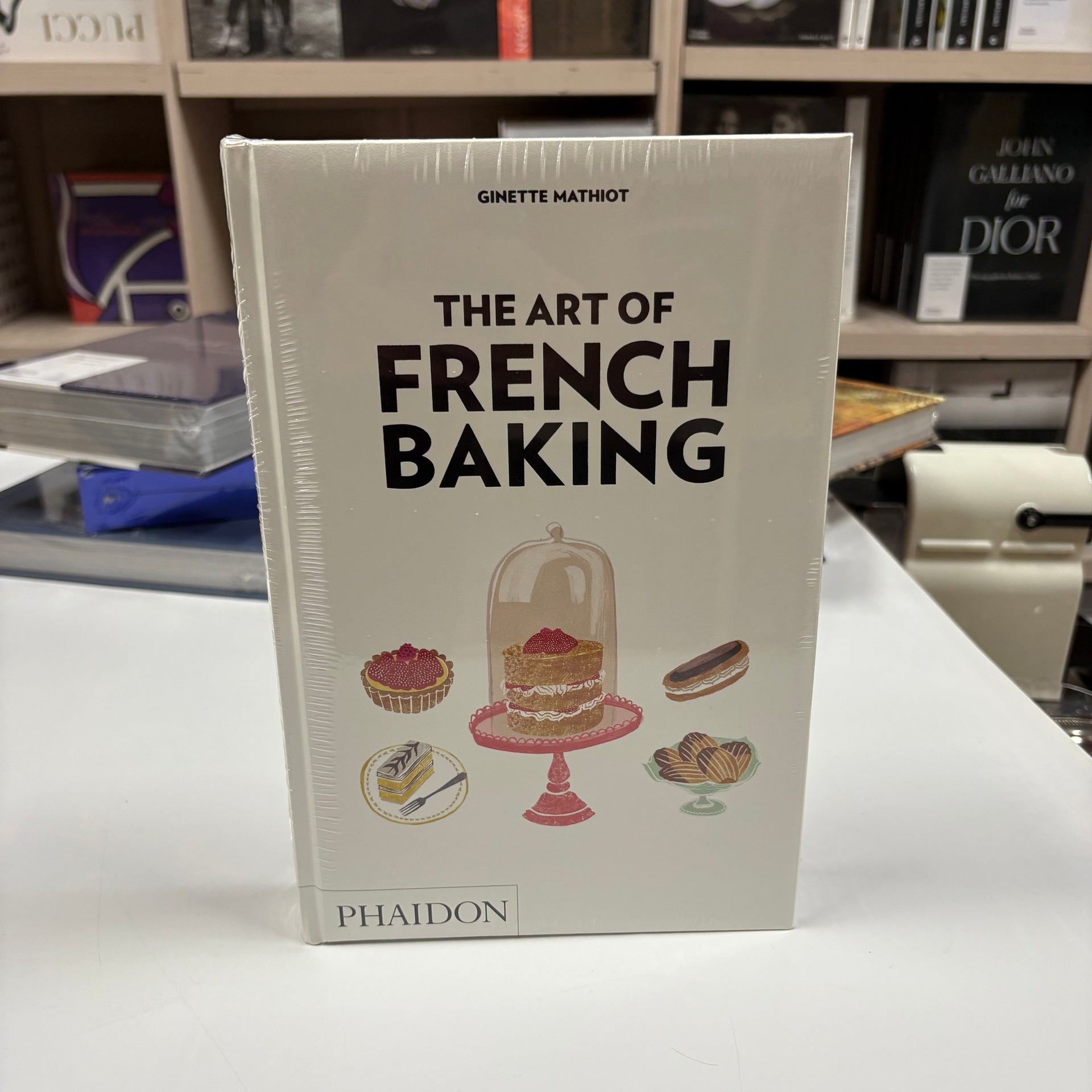 Livro de luxo The Art of French Baking aberto em página de receita, sobre mesa rústica com ingredientes de confeitaria france