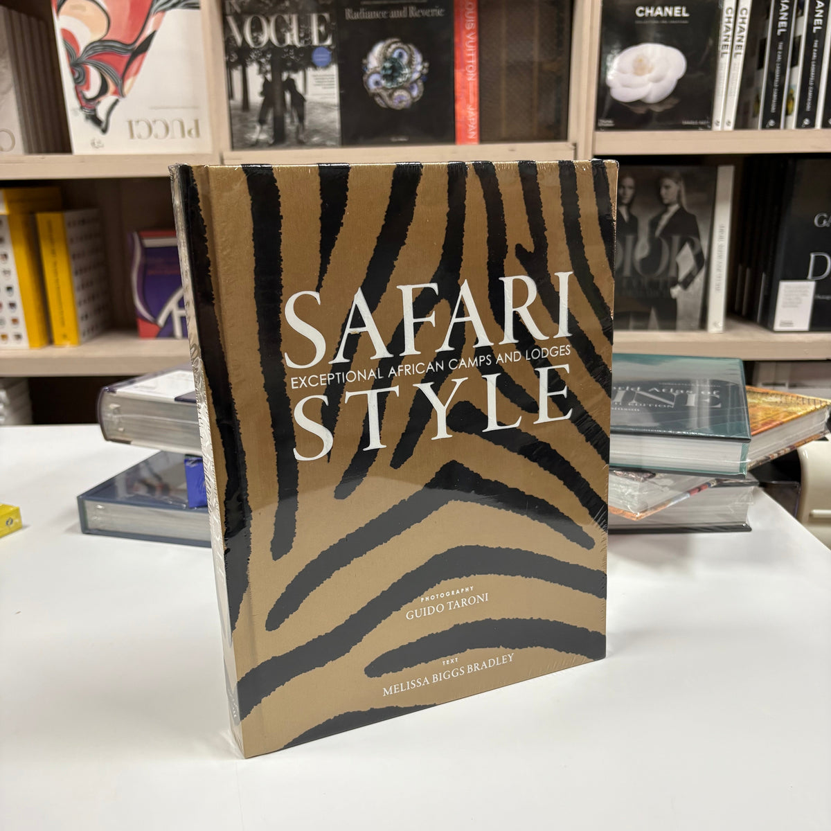 Livro Safari Style com capa dura sobre mesa de centro de madeira rústica, ao lado de uma vela acesa e um globo terrestre anti