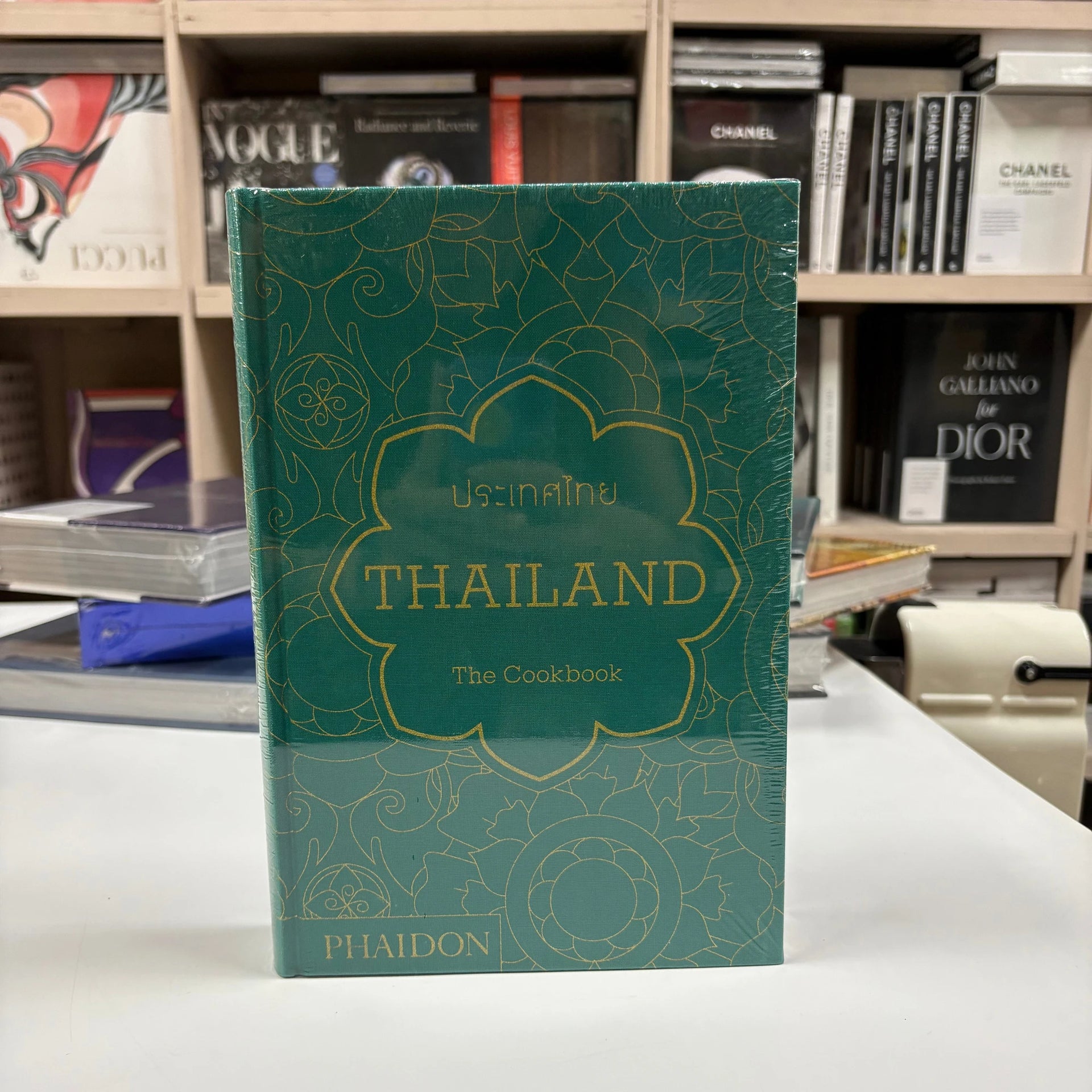 Livro Thailand: The Cookbook Phaidon Press com capa dura colorida sobre mesa de centro de madeira ao lado de utensílios de co