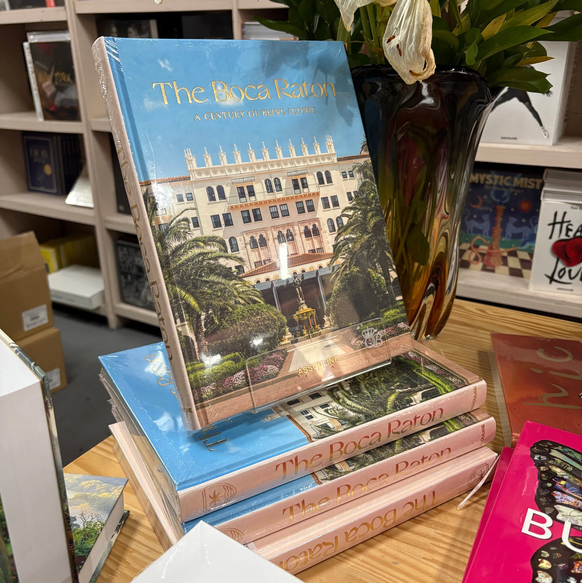 Livro The Boca Raton Assouline com capa dura em tons claros sobre mesa de centro de madeira nobre em sala de estar sofisticad